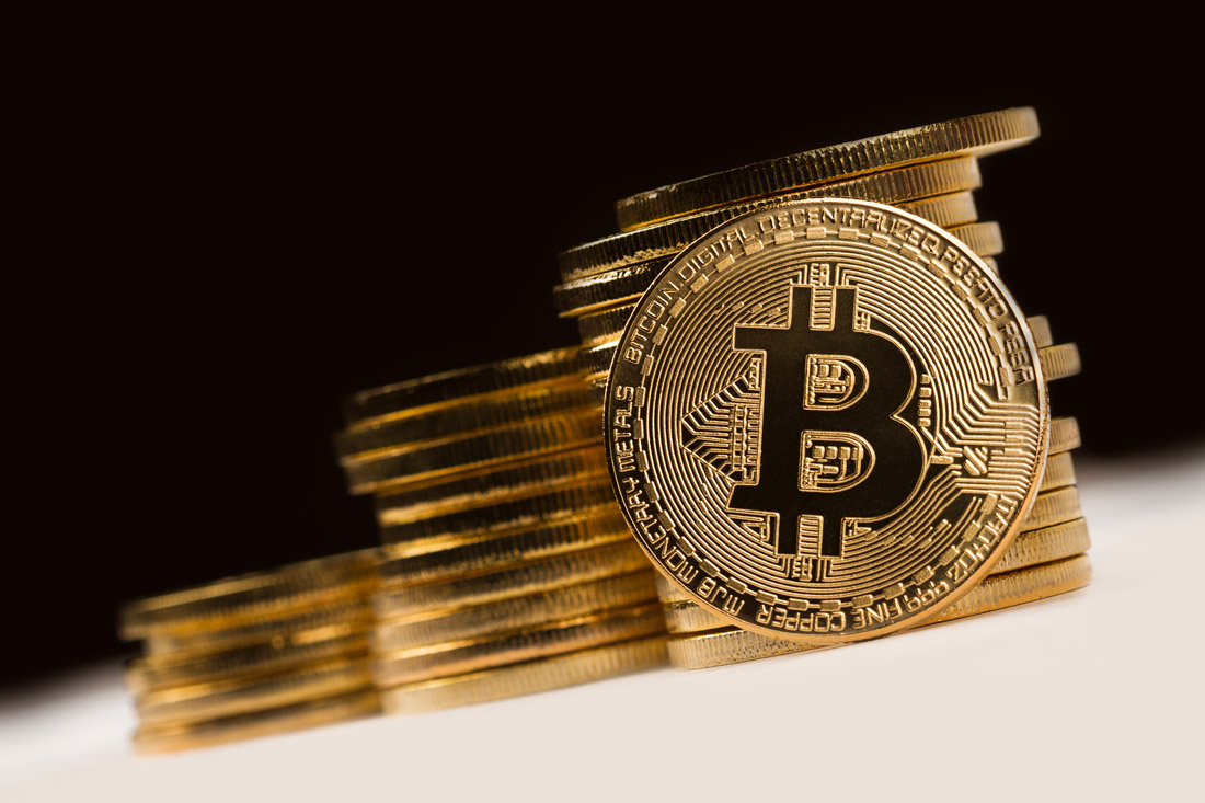 Bitcoin Münze im Vordergrund mit vielen gestapelten Goldmünzen im Hintergrund.